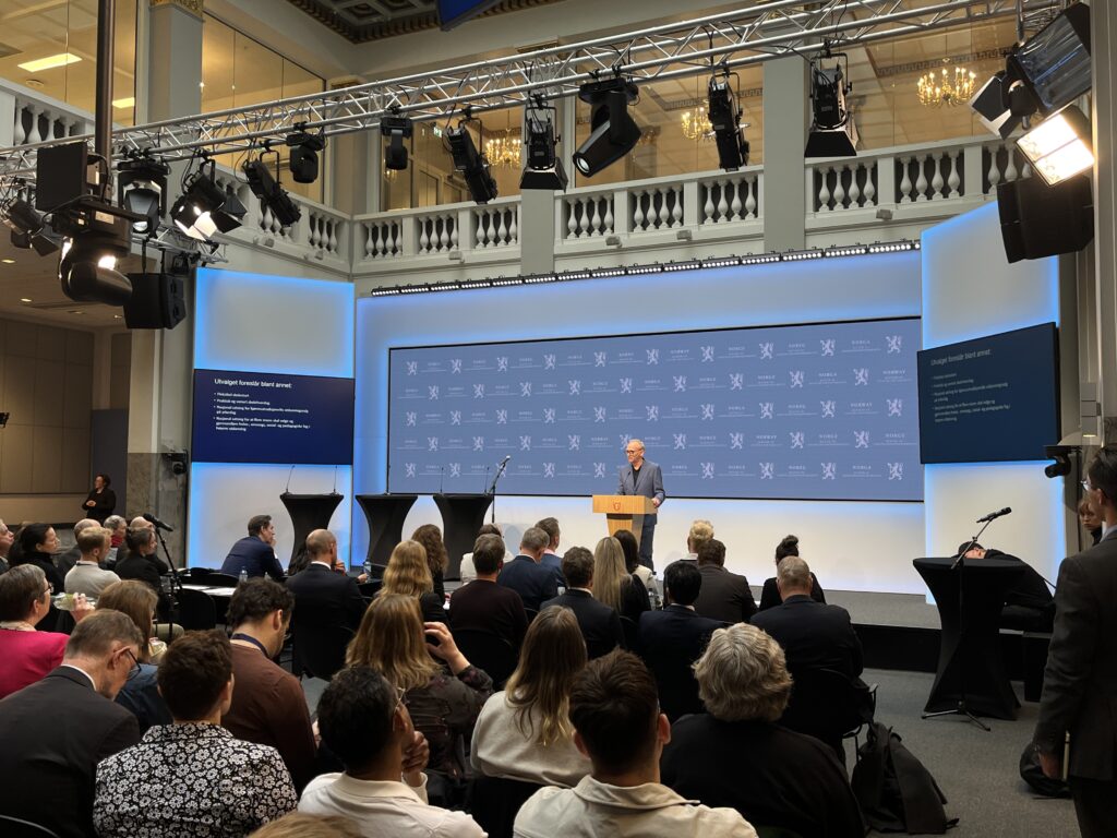 Pressekonferanse. En stor scene i enden og mange i publikum, sittende. Foto