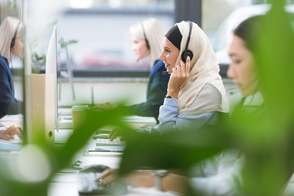 Tre kvinner, en av dem med hijab sitter på et sentralbord og snakker i telefon mens de ser på datamaskin. Foto