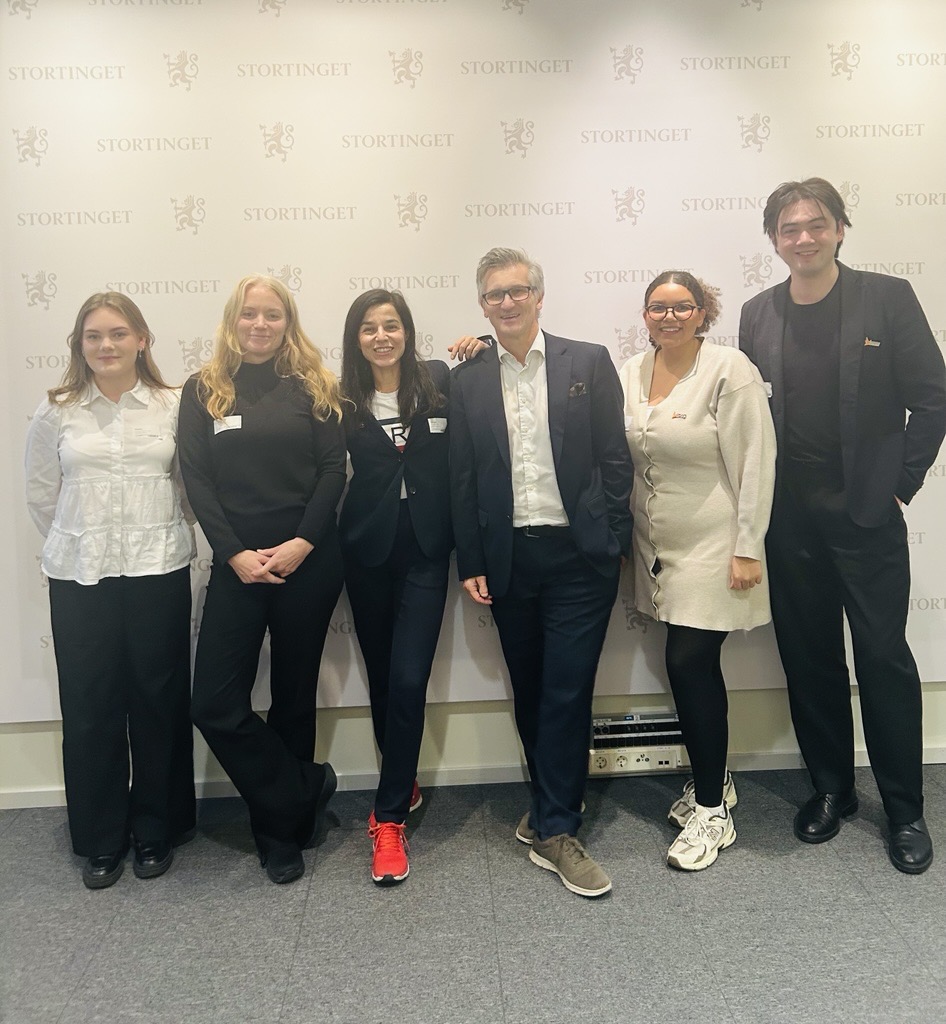 Seks mennesker står å poserer foran en vegg med Stortingets logo. I midten står likestillings- og diskrimineringsombud Bjørn Erik Thon.