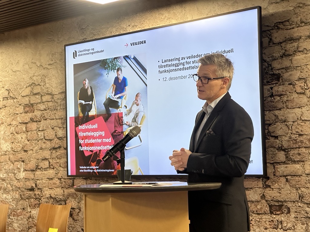 Ombud Bjørn Erik Thon, kledd i svart dress og hvit skjorte, står foran en skjerm og snakker om nylansert rapport. Foto