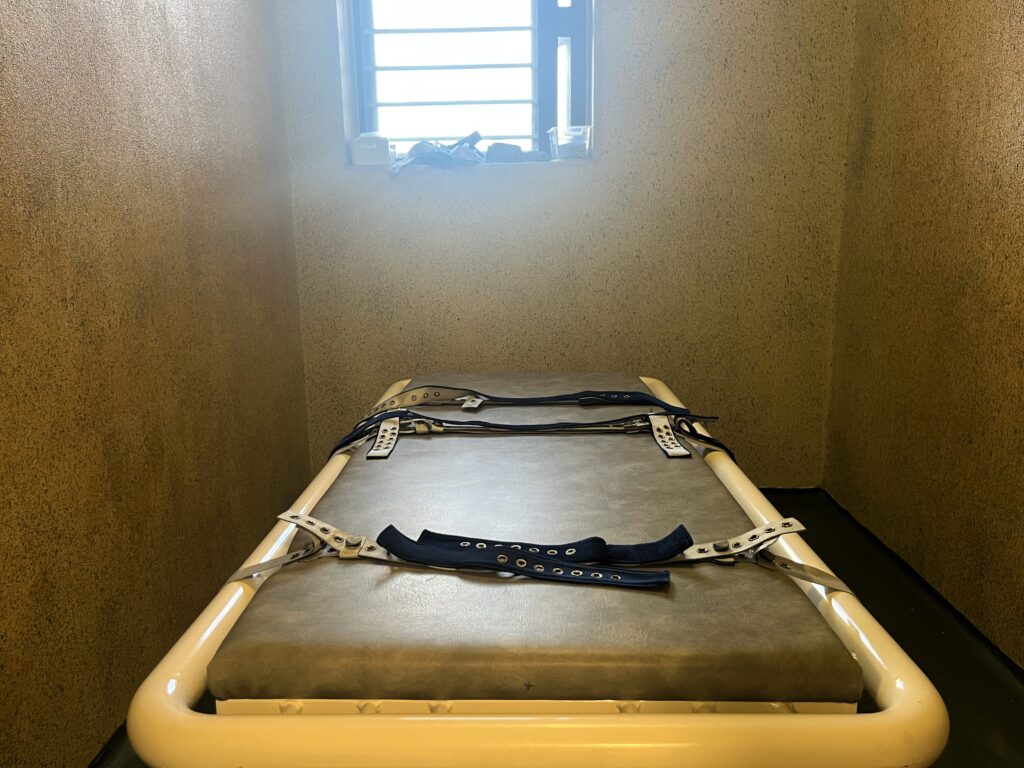 Belteseng inne i en trang fengselcelle med gittervindu i bakgrunnen. Foto