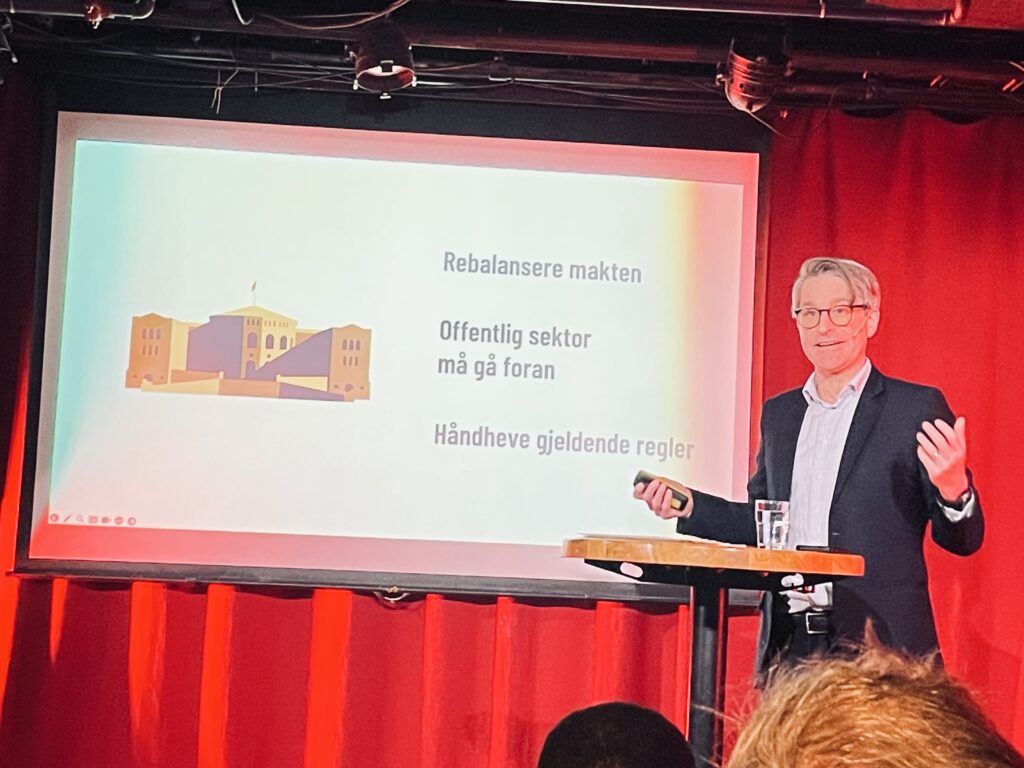 Finn Myrstad, fagdirektør i Forbrukerrådet iført hvit skjorte og svart dressjakke presenterer en rapport foran en storskjerm. Foto