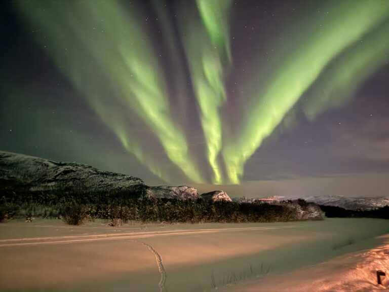 Vakkert og snødekket fjellandskap i Alta lyses opp av grønt nordlys. Foto