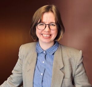 Aurora Nilsen, politisk rådgiver i Likestillings- og diskrimineringsombudet. Aurora har midtskille, hår ned til skuldrene, runde briller og har på seg blå skjorte og grå dressjakke. Foto