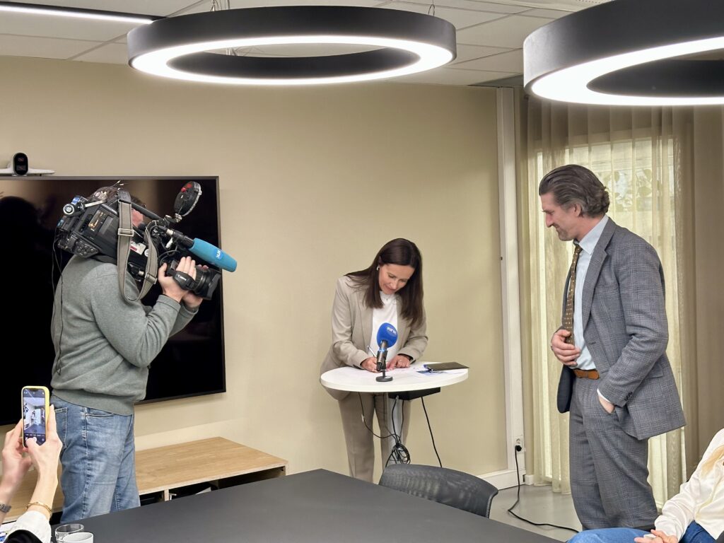 Fiskeriminister Marianne Sivertsen Næss skriver under på samarbeidsavtalen for økt likestilling i fiskerinæringen, mens NRK filmer henne og fagdirektør Lars Kolberg fra LDO ser på. Foto