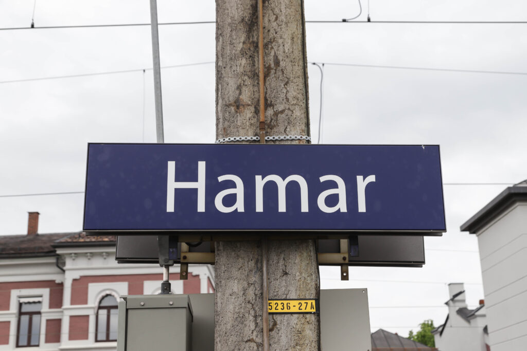 Blått skilt med hvit skrift på en stolpe som det står Hamar på. Foto