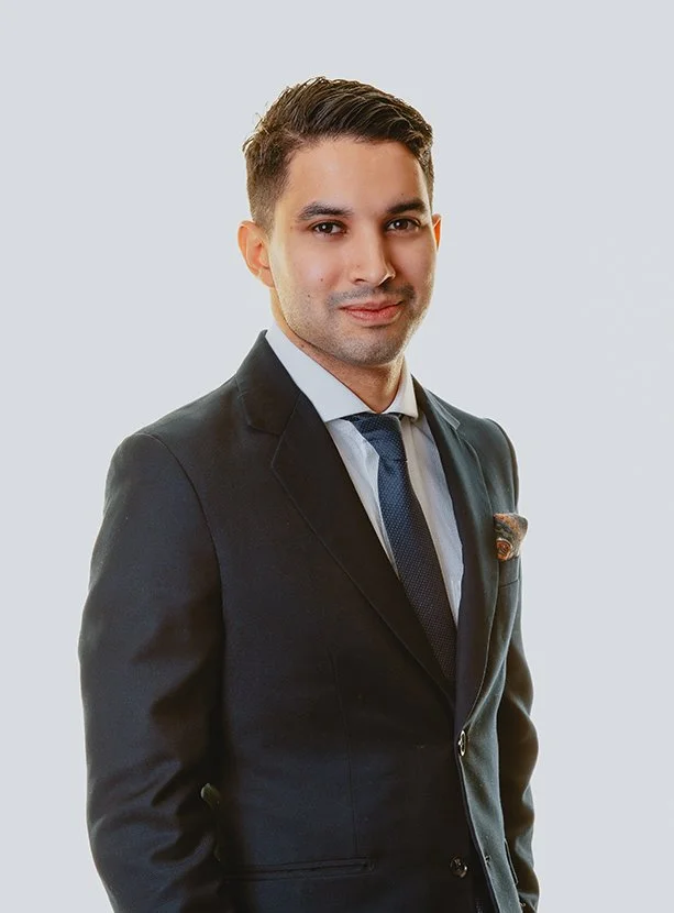 Bildet er av en mann med kort, mørkt hår som ser inn i kameraet. Han har på seg dress og slips, med hvit skjorte inni. Bildet har grå bakgrunn. Mannen er Alexander Gonsalo Sele, advokat.