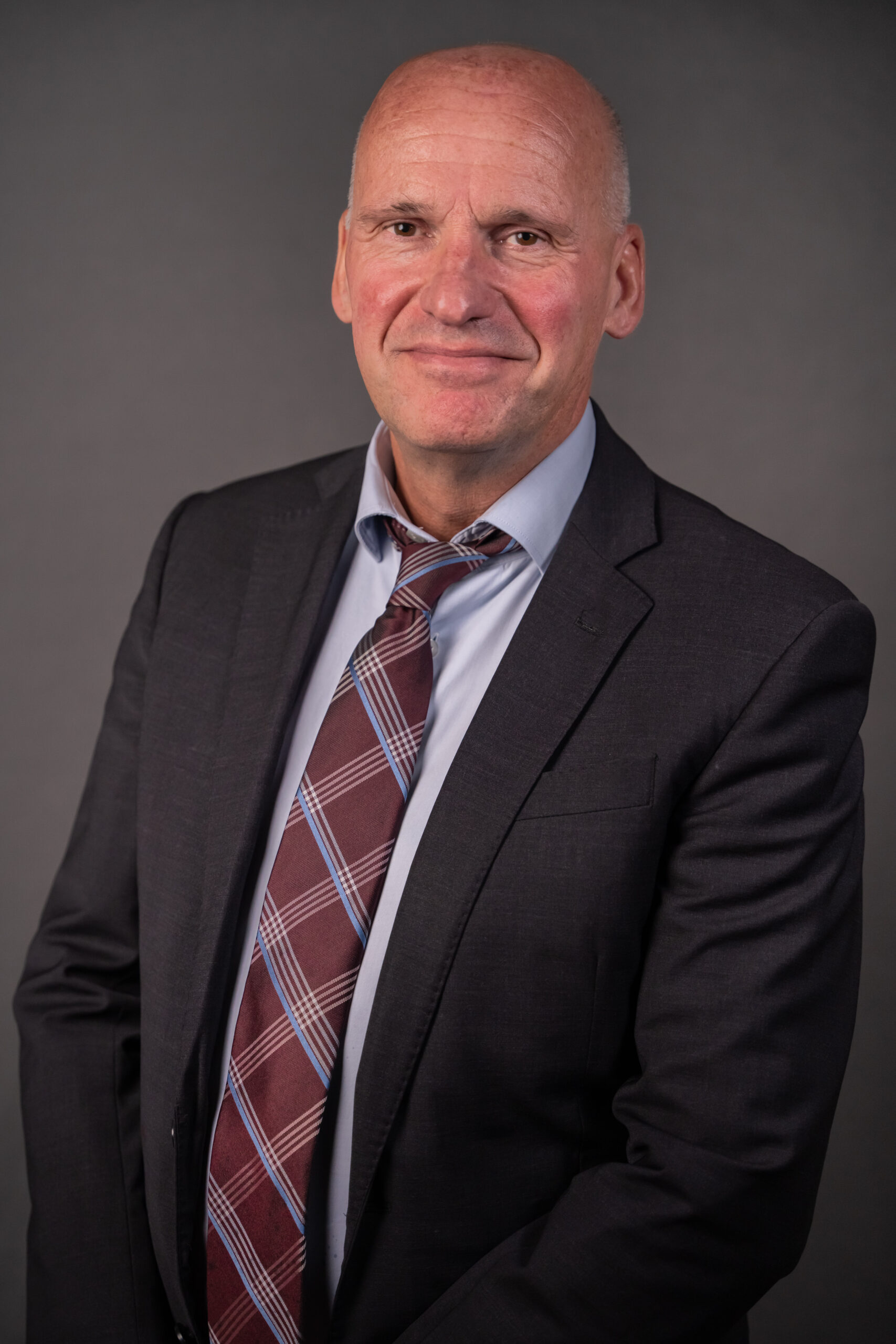 Bildet er av en skallet mann. Han har på seg sort dressjakke, lyseblå skjorte og rutete slips. Bakgrunnen er mørkegrå. Mannen er Geir Lippestad, advokat.