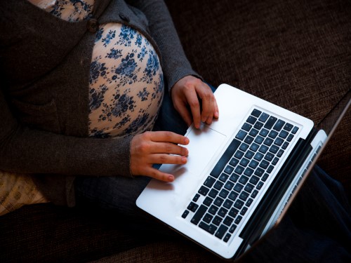 Gravid dame som sitter med en bærbar datamaskin på fanget