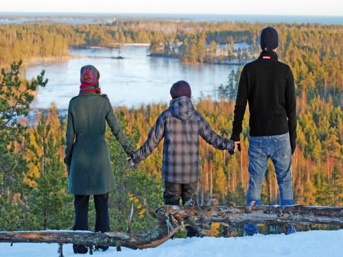 En dame, et barn og en mann holder hender og ser utover et vann og skog